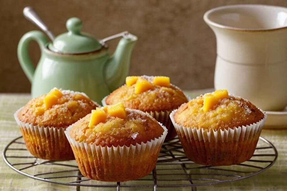 Pineapple banana muffins topped with pineapple pieces on a wire stand, served with a teapot for a cozy breakfast setting
