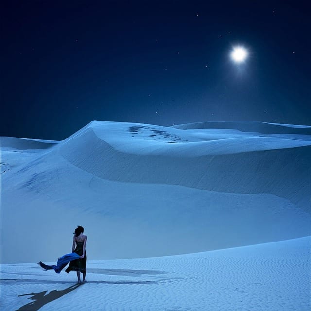 Woman walking on moonlit sand dunes under a bright full moon — procrastination, energy and good timing