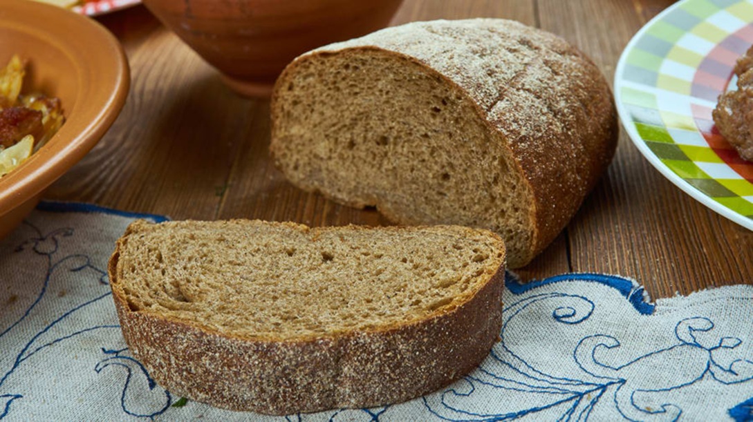 Sliced homemade Swedish Limpa bread showing a dense rye crumb with a crispy crust on a wooden table