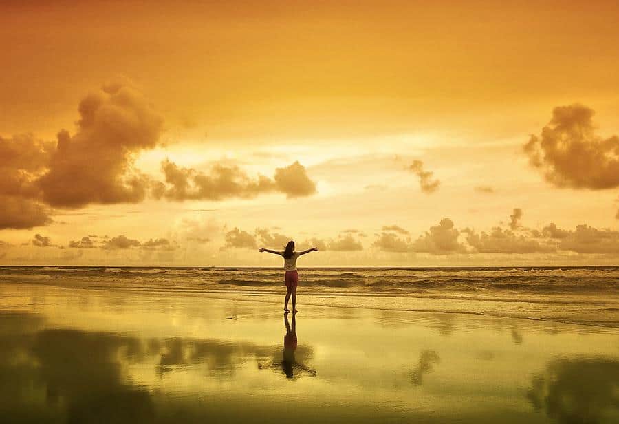 Person standing with open arms on a beach at sunrise, symbolizing trust, surrender, and openness
