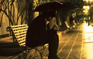 A person sitting alone on a park bench at night under an umbrella, reflecting on connection and solitude.