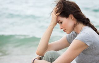 Woman sitting by the ocean, appearing thoughtful and anxious, symbolizing the quiet tension between worry and anxiety.