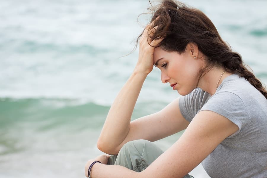 Woman sitting by the ocean, appearing thoughtful and anxious, symbolizing the quiet tension between worry and anxiety.