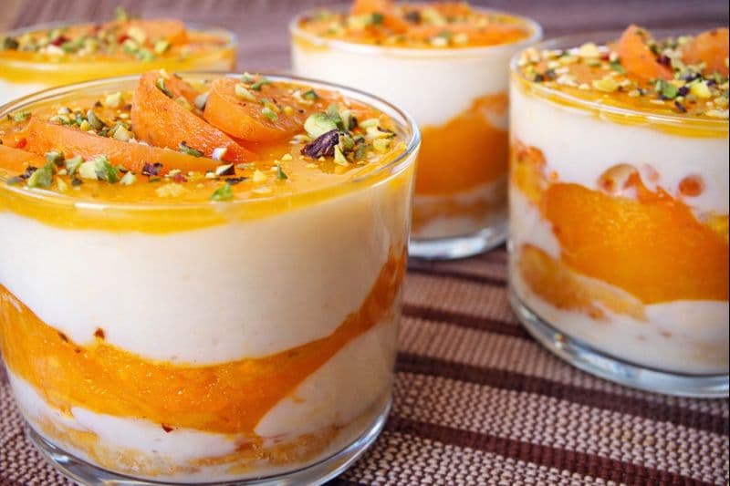 Apricot and amaretto tiramisu layered with mascarpone cream, fresh apricots, and tea-soaked ladyfingers topped with mango coulis and pistachio garnish
