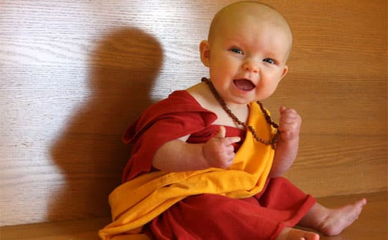 Baby monk smiling in red and yellow robes symbolizing conscious spiritual growth