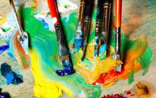 Paintbrushes resting in vibrant paint, symbolizing creative life energy, self-expression, and renewal