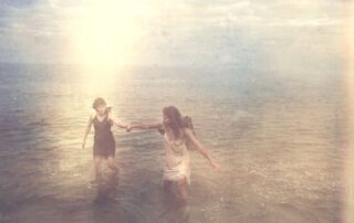 Two women holding hands while walking through water, symbolizing spiritual support, guidance, and shared growth
