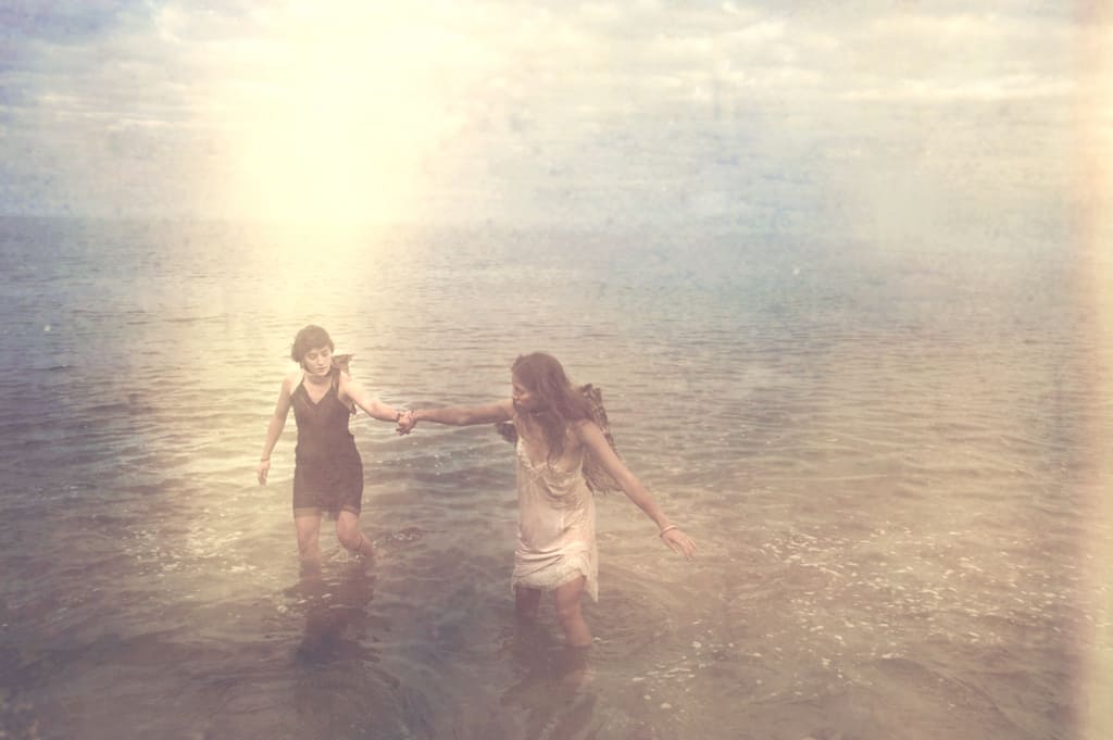 Two women holding hands while walking through water, symbolizing spiritual support, guidance, and shared growth