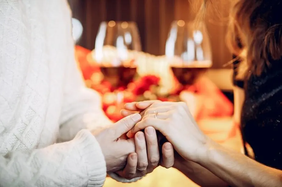 Couple holding hands across a romantic table setting, symbolizing love and emotional connection.