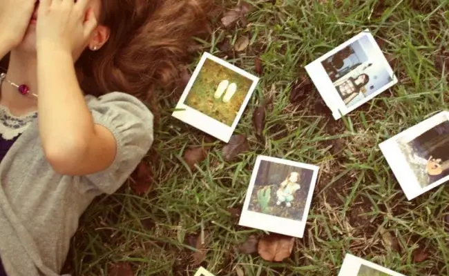 Woman lying on grass surrounded by old relationship photos, covering her face