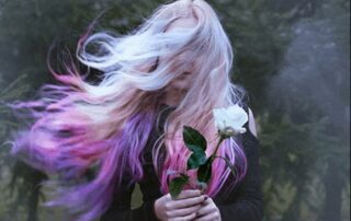 Person holding a white rose with flowing hair, symbolizing self-awareness, innocence, and releasing assumptions