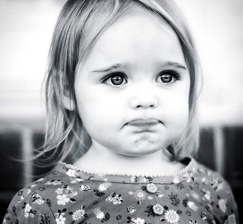 Black-and-white photo of a little girl with a pouty expression, representing the French word “moue” — a slight grimace or pout.
