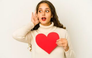 Woman holding a red heart and listening inwardly, symbolizing the heart speaking for the soul