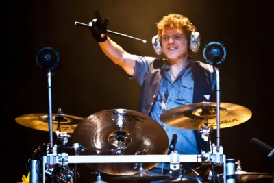 Rick Allen performing live on drums with Def Leppard after his accident, holding drumstick aloft