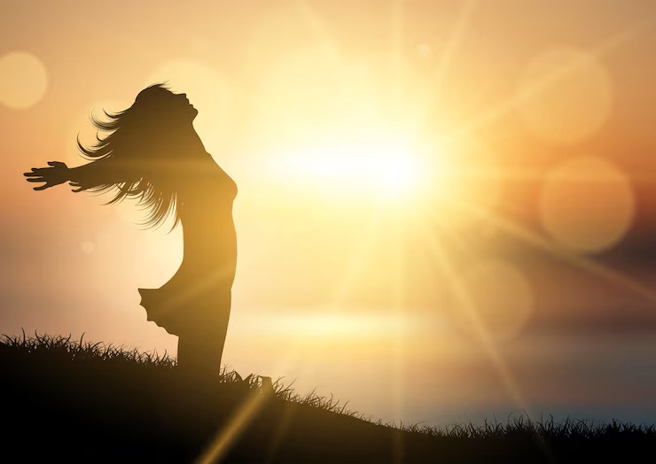 Silhouette of a person standing with open arms in sunlight, symbolizing soul growth and self awareness. Shining her inner light.