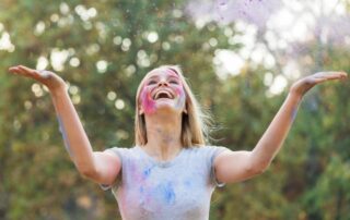Woman smiling joyfully with colorful paint on her face, symbolizing authenticity, creativity, freedom, and celebration of your true nature.