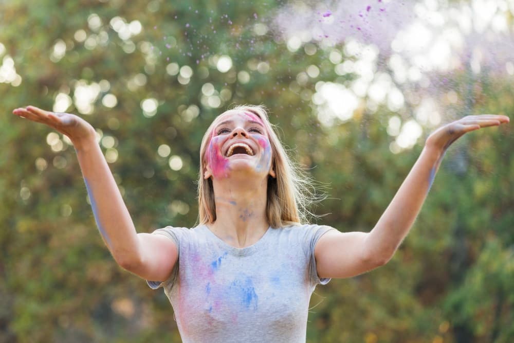 Woman smiling joyfully with colorful paint on her face, symbolizing authenticity, creativity, freedom, and celebration of your true nature.