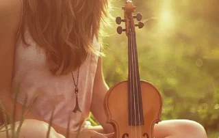 A woman sitting quietly in the light with a violin, symbolizing how spiritual practice reshapes perception and reveals the unity of material and sacred worlds.