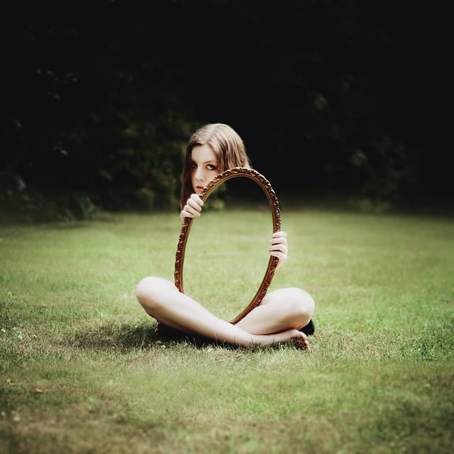 Woman sitting on grass holding an empty mirror, symbolizing self reflection, emotional awareness, and life lessons