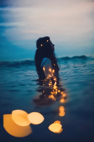 Woman standing in calm water surrounded by soft lights, symbolizing spiritual renewal and inner reflection